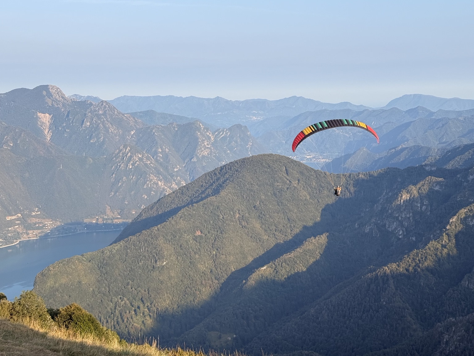 A tandem paraglider pilot flying above a lake and mountains